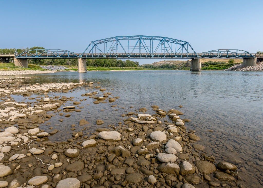 A river with rocks in the foreground and an old bridge in the background. Ethno tourism