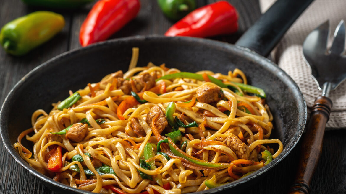 A pan of noodles with meat and peppers.