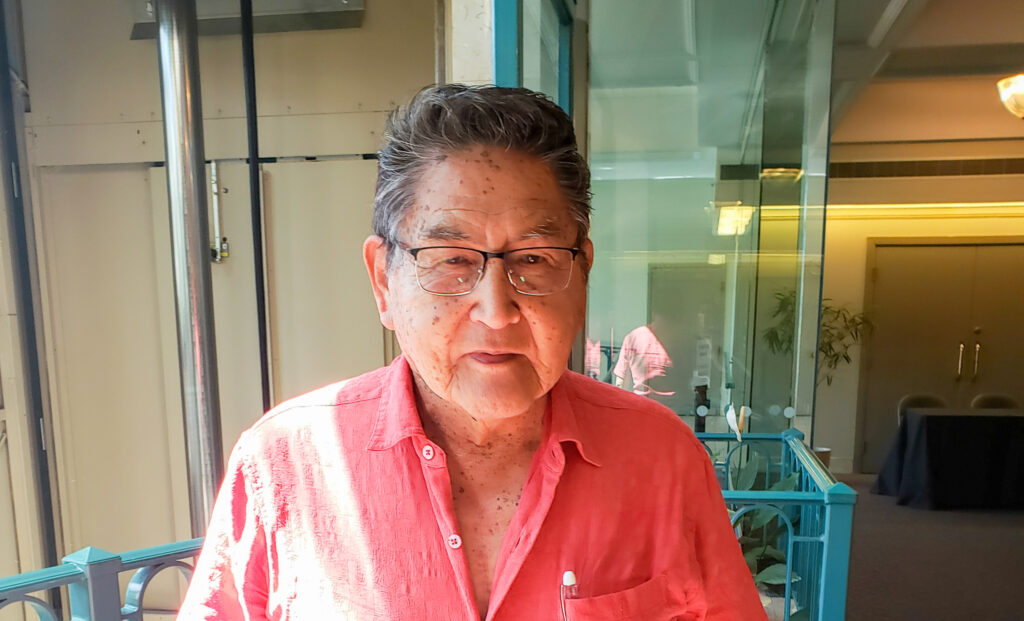 A man in a red shirt is standing by some glass.