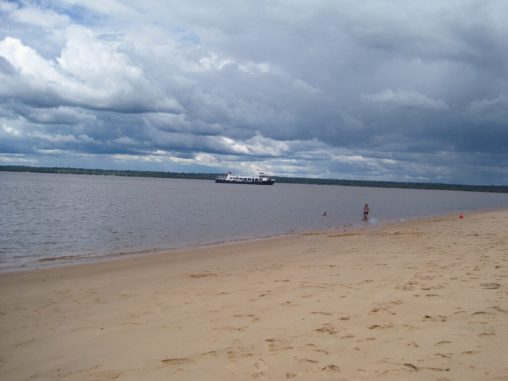 A beach with people walking on it and a boat in the water.