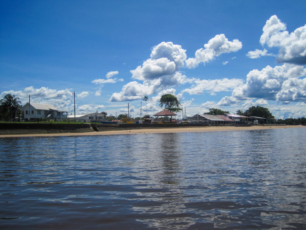 A body of water with a beach and some houses in the background.