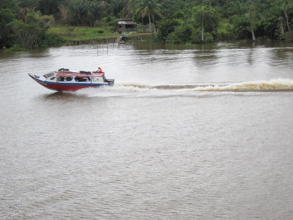A boat traveling down the river with trees in the background.