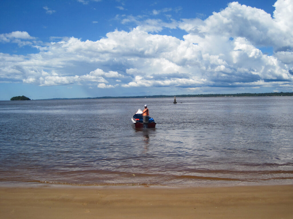 A boat traveling down the river with trees in the background.