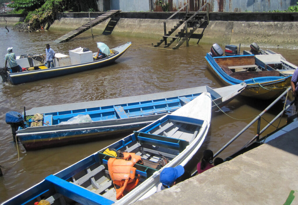 A boat traveling down the river with trees in the background.