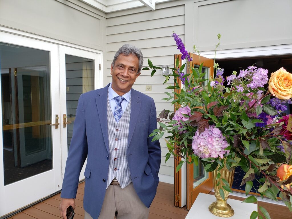 A man in a suit standing next to a flower arrangement.