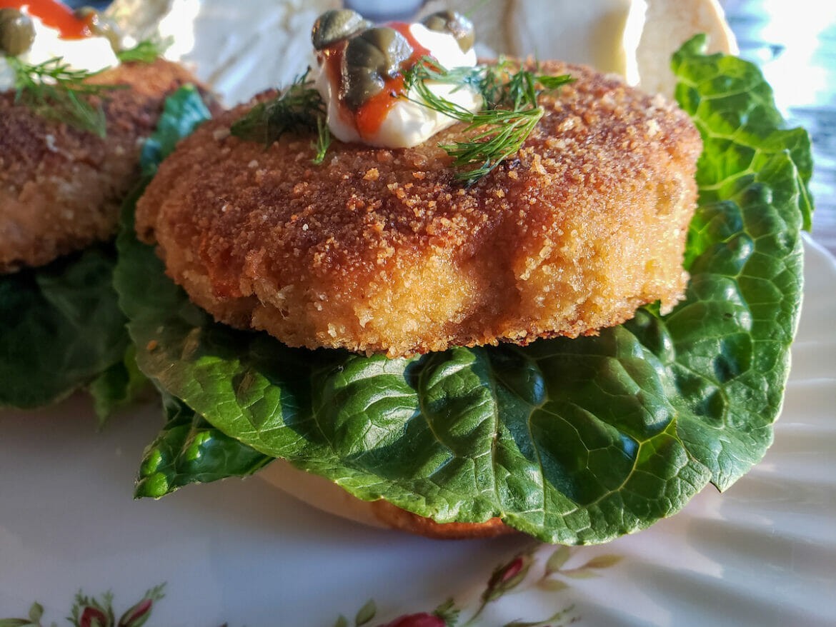 A fish cake and bread sandwich with lettuce and a decorative ornament on top.