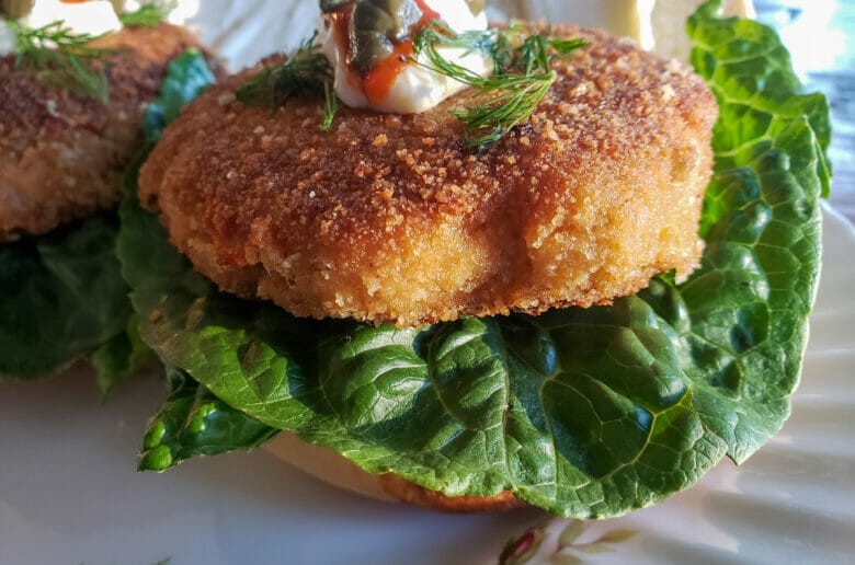 A fish cake and bread sandwich with lettuce and a decorative ornament on top.