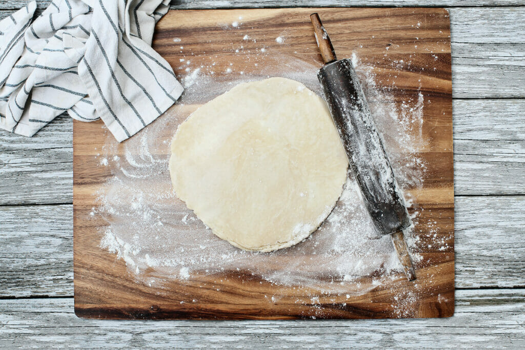 A wooden cutting board with dough and a knife.