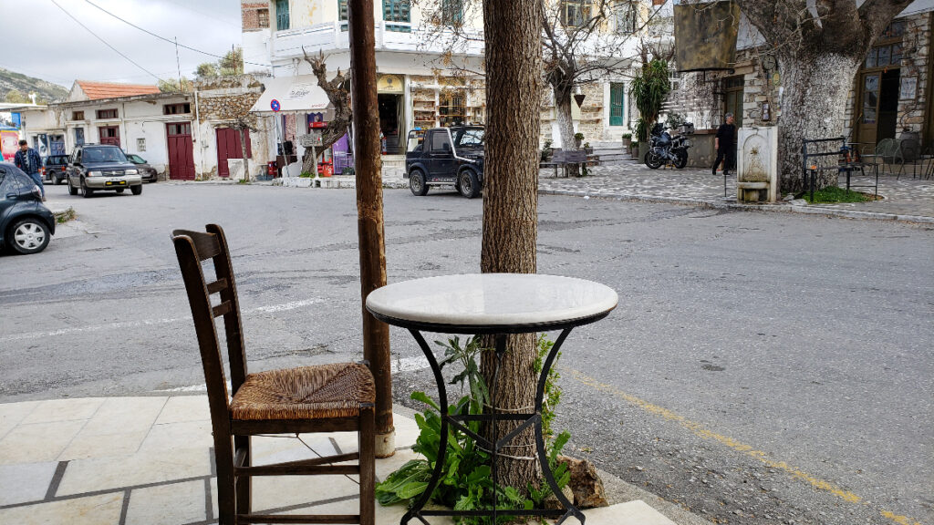 A table and chair on the sidewalk of an empty street.