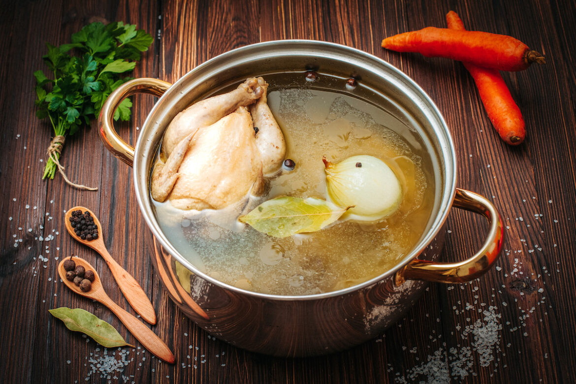 A pot of chicken and broth on the table.