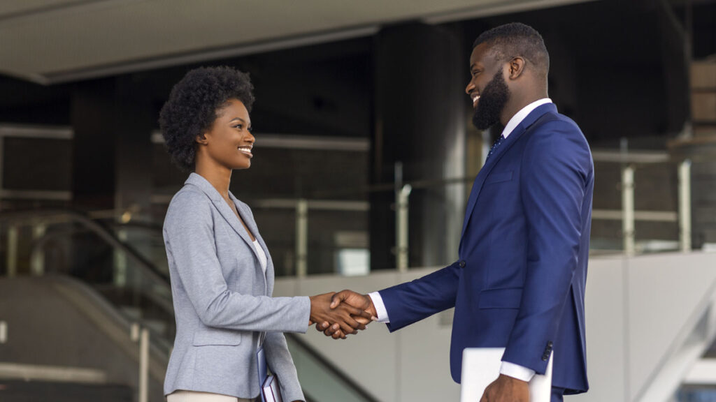 A man and woman shaking hands in front of some stairs.